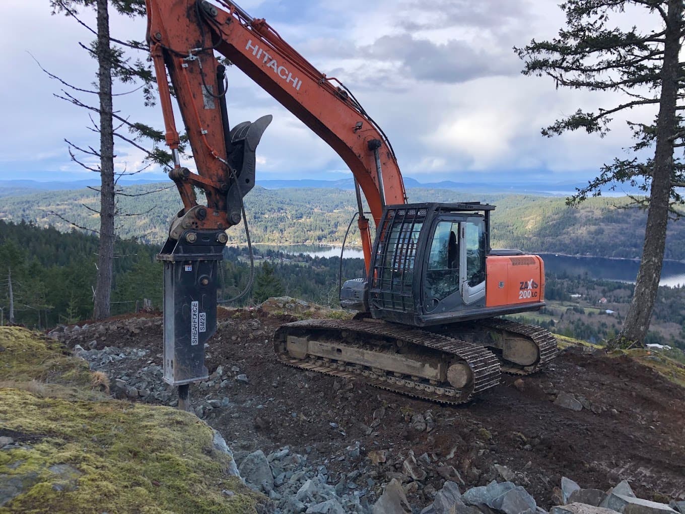A Shearforce hydraulic breaker mounted on an excavator, with the island and sea behind