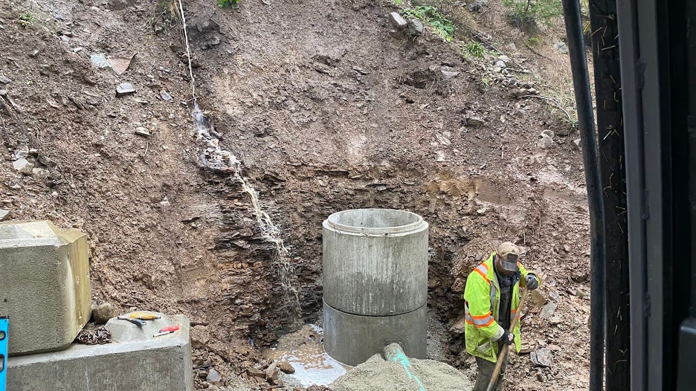 A worker setting a concrete chamber into a wet cut bank with water running through