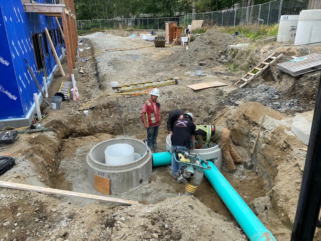 A crew setting concrete manhole sections and a large sewer main into an open trench