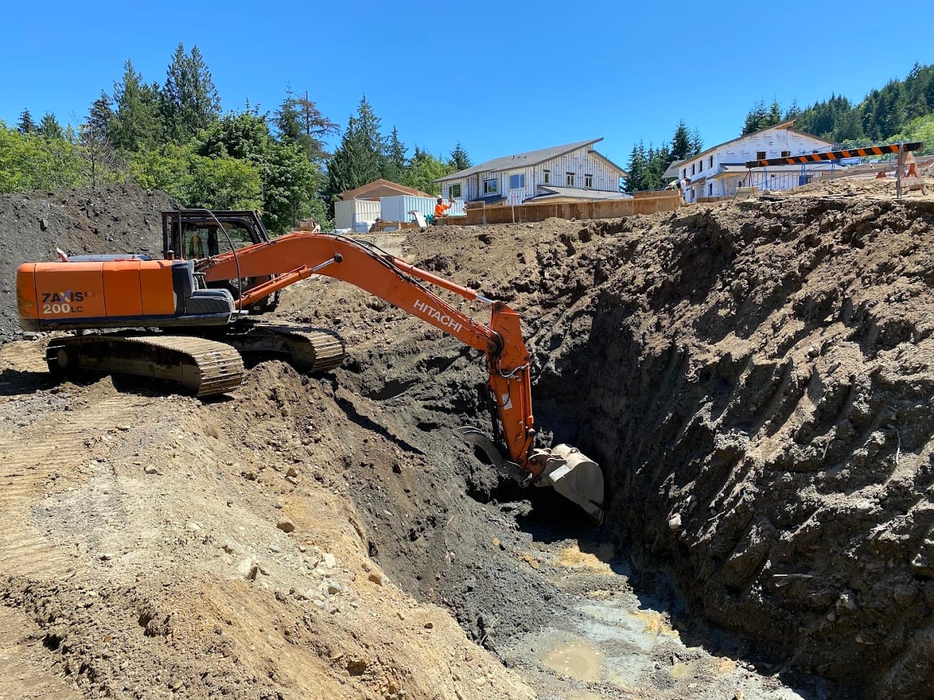 A deep foundation trench dug beside houses under construction on Salt Spring Island